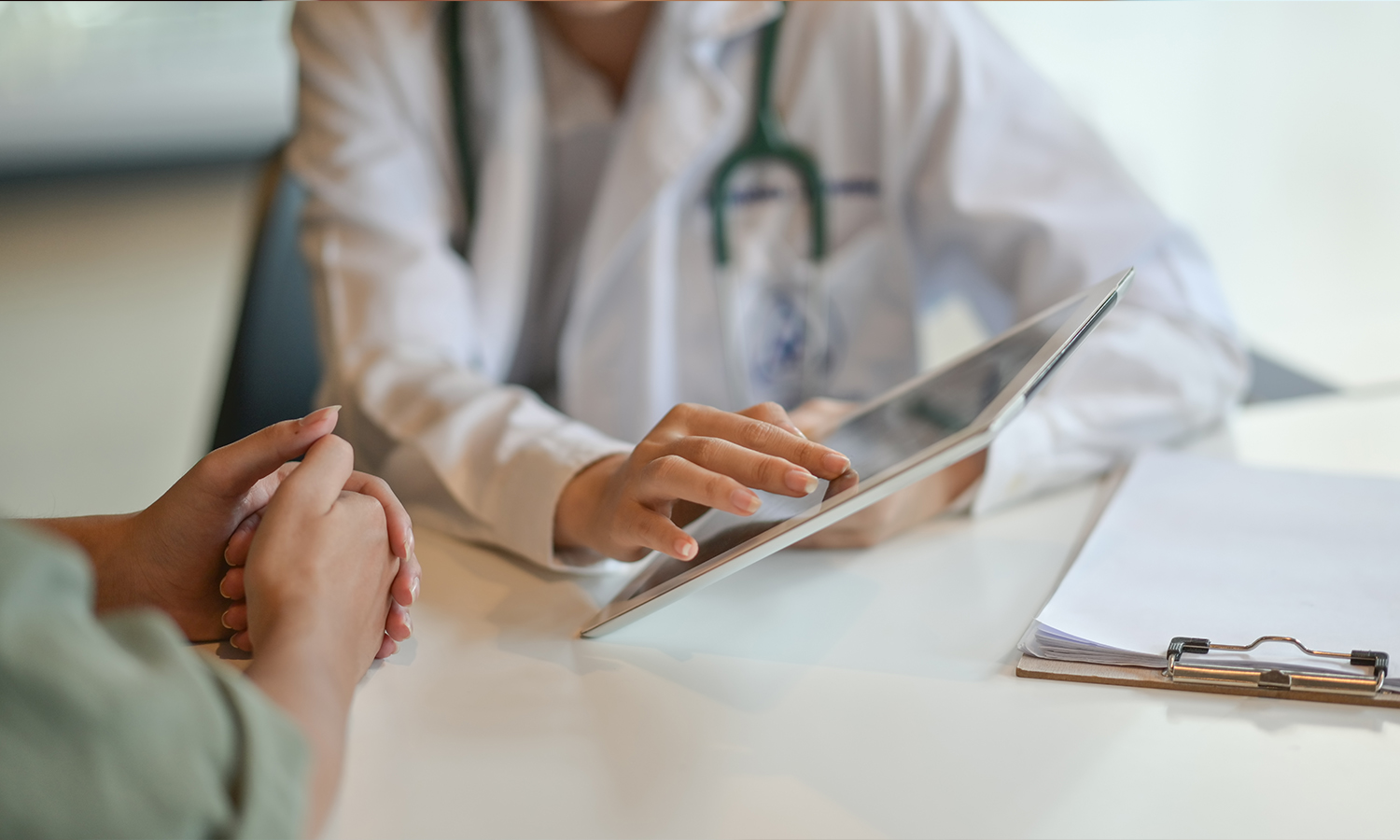 A healthcare practitioner uses an electronic device while speaking with a patient.